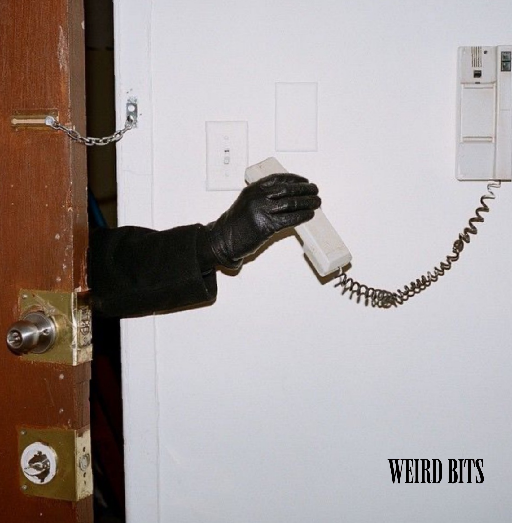 Gloved hand on an intercom beside a Weird Bits poster
